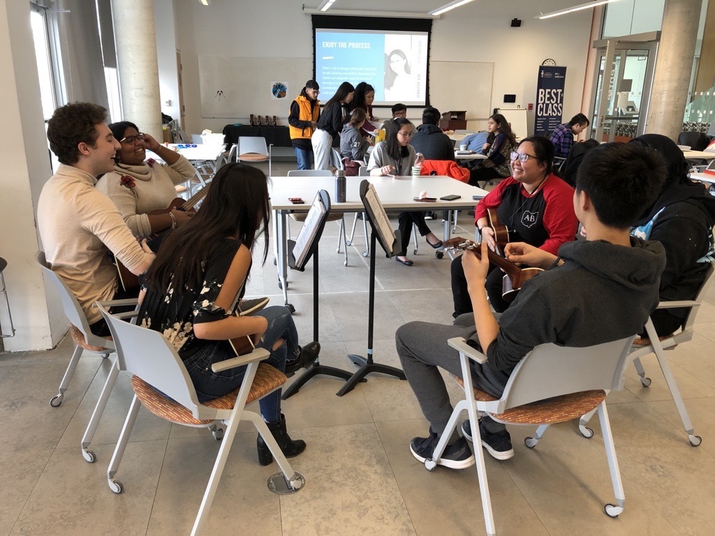 A group of students sitting in a circle playing ukuleles.